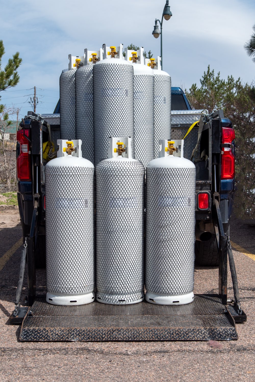 A truckload of large propane cylinders on a pickup lift-gate, ready for delivery across the Denver metro area